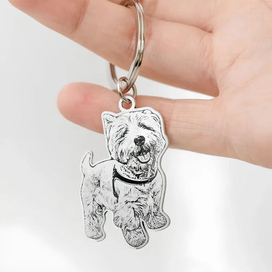 A hand holding a silver metal keychain featuring an engraved West Highland Terrier dog silhouette, shown against a plain white background.