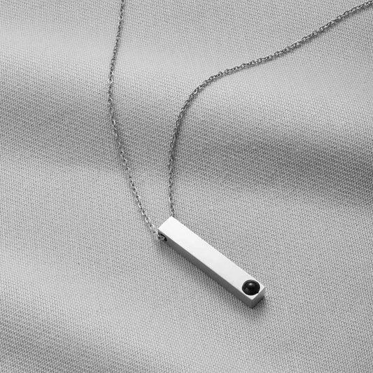 Silver necklace with a bar pendant on a light gray fabric background