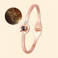 A slim rose gold bangle bracelet with a circular bezel-set black gemstone and a small clear stone, shown on a light beige background with a circular inset detail of the inner band pattern.