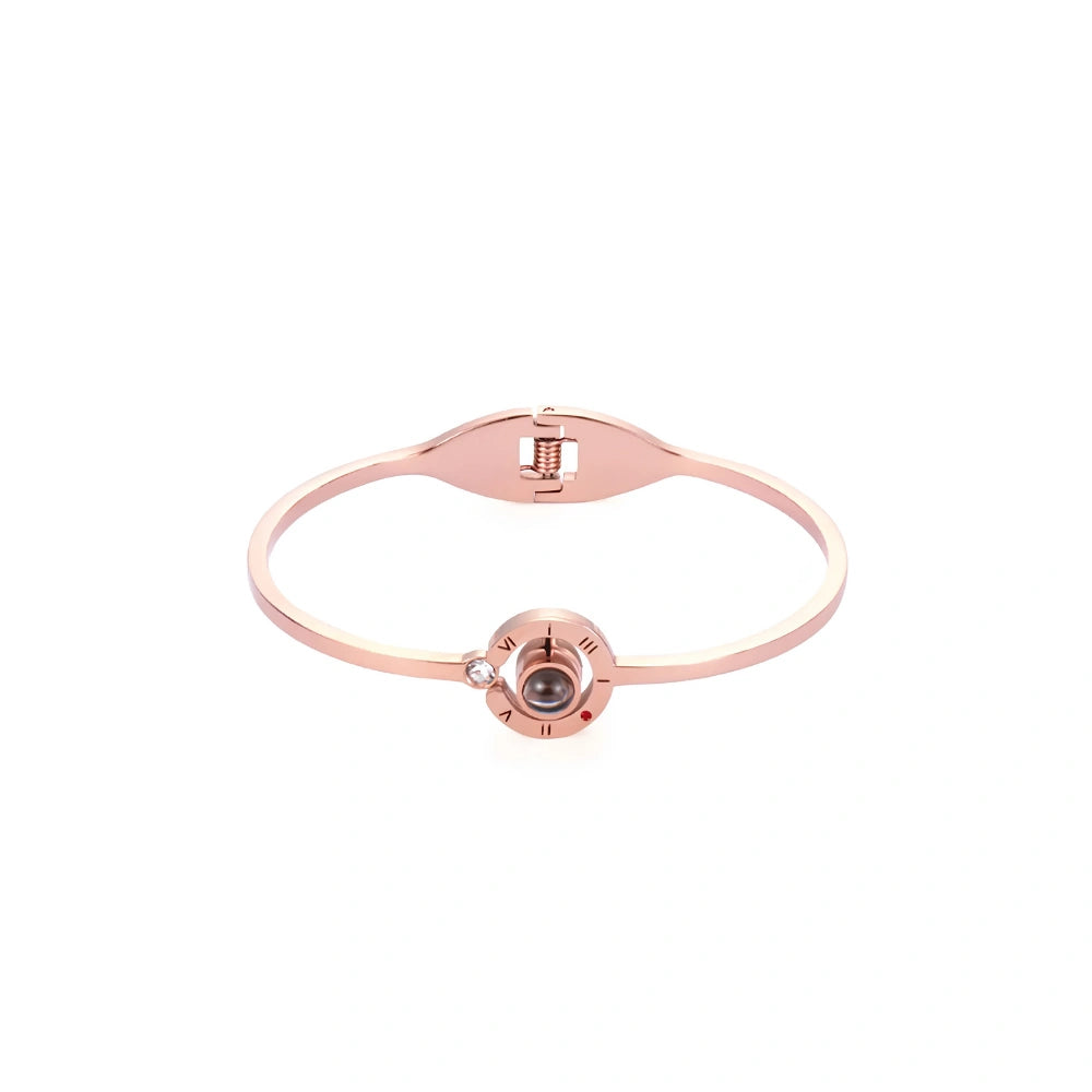 A rose gold bangle bracelet with a central compass design featuring a dark brown gemstone and a small clear accent stone, shown on a plain white background.