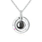A silver pendant necklace featuring a double-ring design with a central dark gray sphere, a small pink gemstone, and a pavé-set clear crystal accent. The pendant is shown on a white background with a subtle reflection.