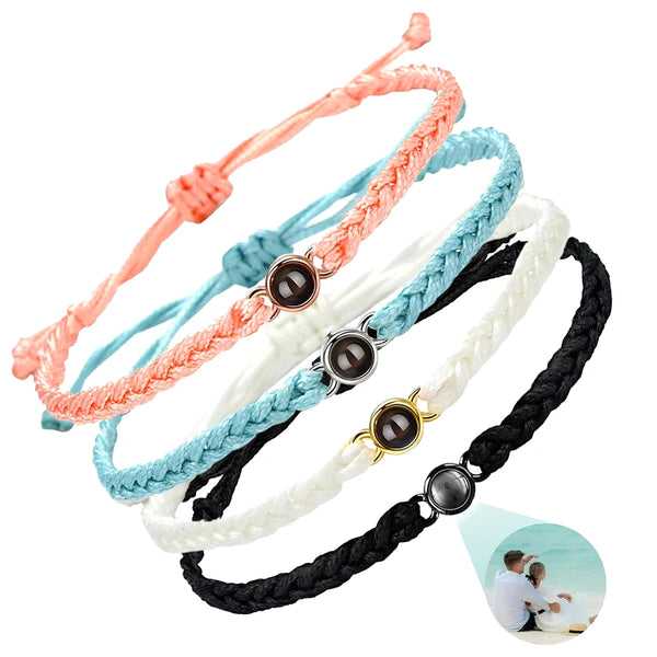 Four braided cord bracelets in peach, light blue, white, and black, each featuring a round dark stone centerpiece with a small metallic bezel. A circular inset at the bottom right shows a couple photo projected on one of the bracelets.