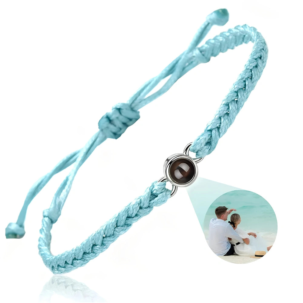 A light blue braided cord bracelet with an adjustable sliding knot and a central silver-toned bezel holding a dark oval stone. A photo projection of a couple