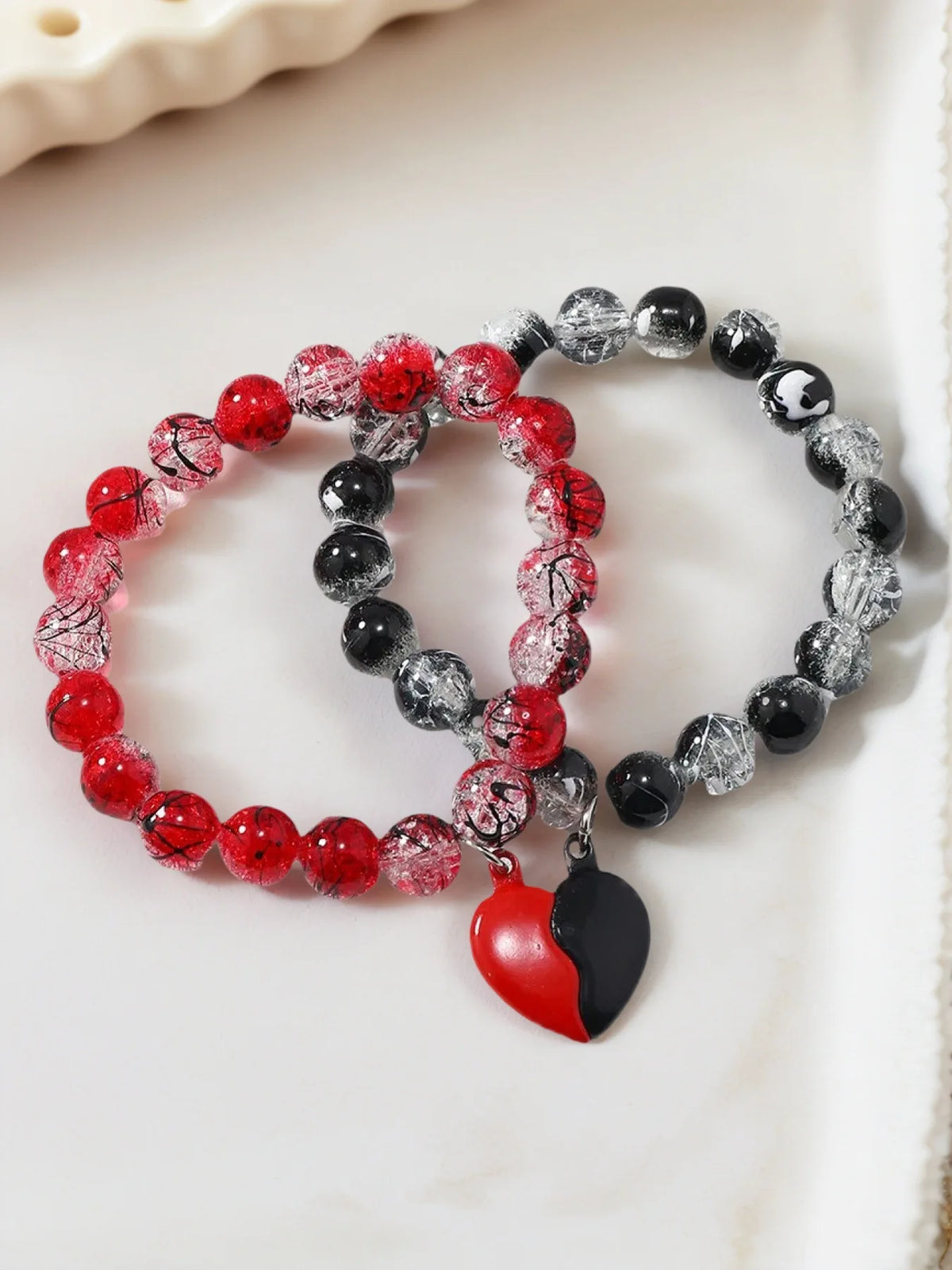 Two beaded bracelets with red, black, and clear beads, and a heart charm on a light background.