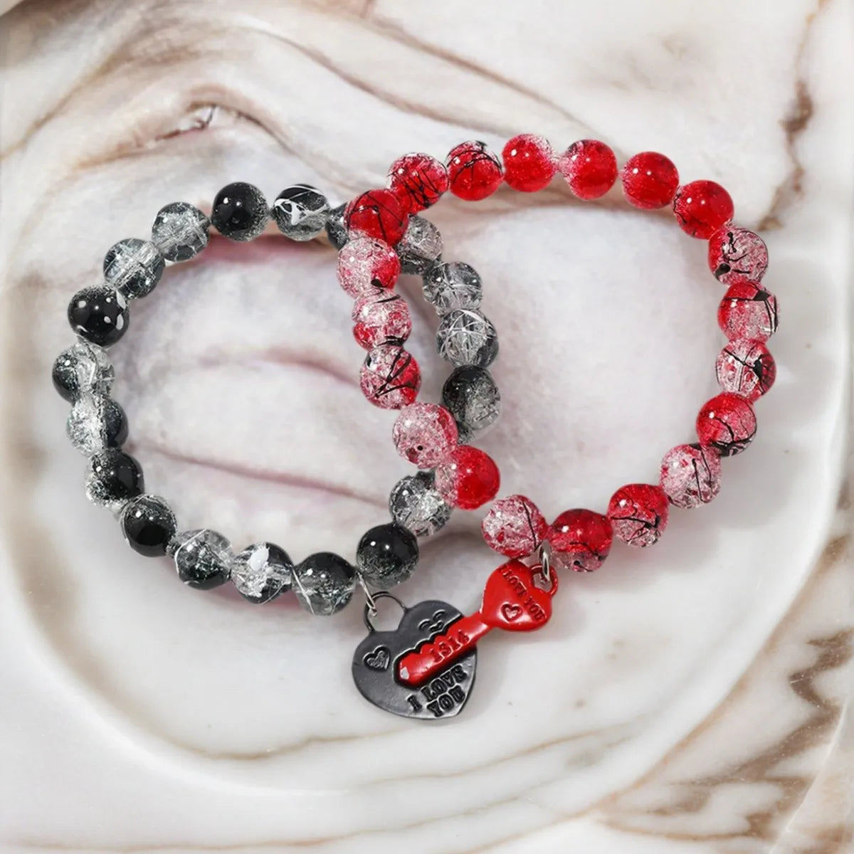 Two beaded bracelets with red, gray, and black beads on a marble surface.