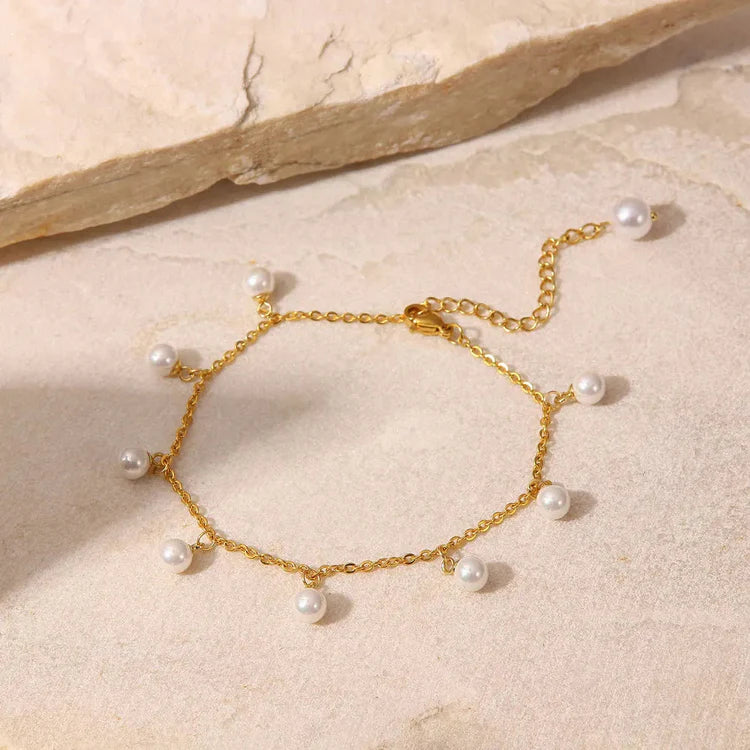 Gold bracelet with pearls on a beige stone surface