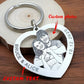 A heart-shaped silver metal keychain with engraved custom text and a custom photo of a couple, displayed on a wooden surface with a wood slice prop. 