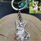 A metal keychain with a engraved corgi dog pendant, displayed on a round wood slice. A small inset photo in the top right shows a real corgi outdoors, demonstrating how the pet photo is used for the engraving.