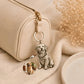 A cream-colored leather zippered pouch with a gold-tone zipper, featuring a custom engraved metal keychain charm shaped like a sitting golden retriever dog. The charm includes a small circular inset showing the reference photo of the dog used for the engraving.