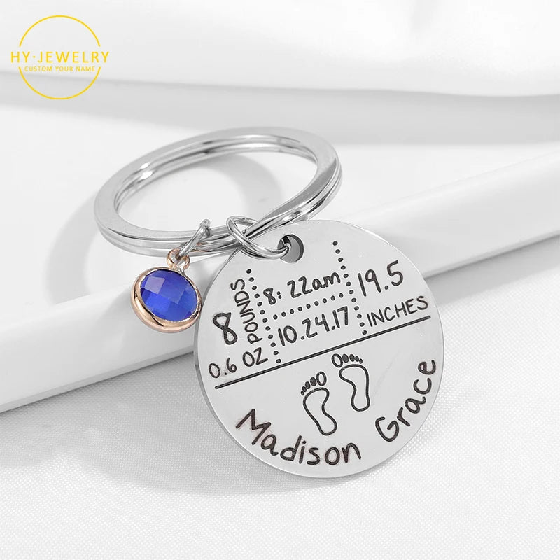 Silver keychain with engraved baby details and blue gemstone on a white background