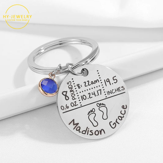 Silver keychain with engraved baby details and blue gemstone on a white background