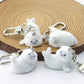 Four white fluffy keychains shaped like dogs on a wooden surface.