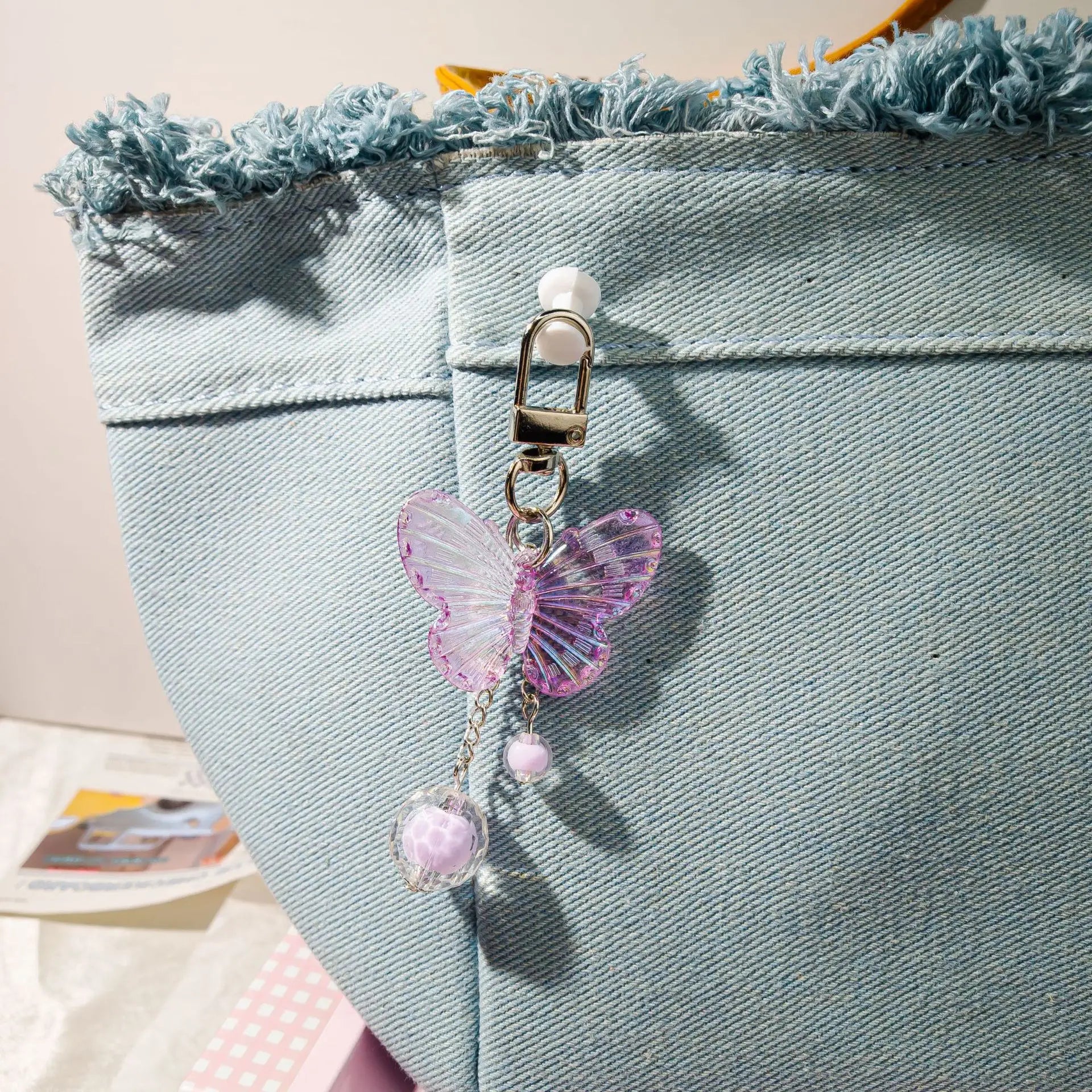 Butterfly-shaped keychain attached to a denim bag with a blurred background