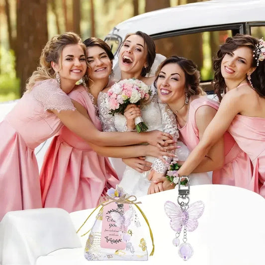 Bride with bridesmaids in pink dresses in front of a white car, with a decorative bottle and butterfly charm in the foreground.