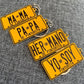 Yellow license plate keychains with black text on a gray textured background