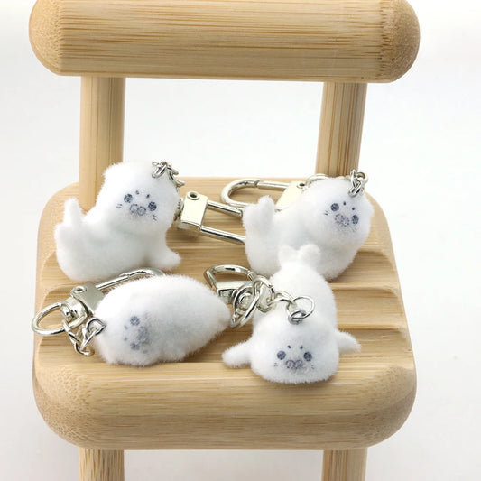 Four white fluffy keychains with small gray faces on a wooden stool.