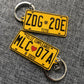 Two yellow license plate keychains on a gray textured background