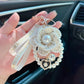 Hand holding a decorative keychain with pearls and a heart charm in a car interior.