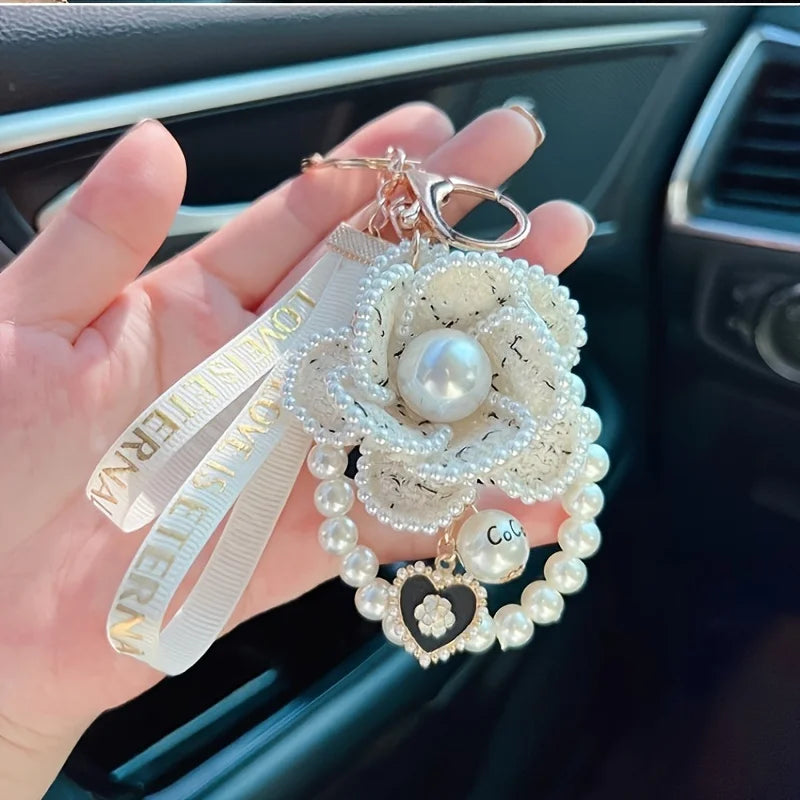 Hand holding a decorative keychain with pearls and a heart charm in a car interior.