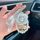 Hand holding a decorative keychain with pearls and ribbons in a car interior.